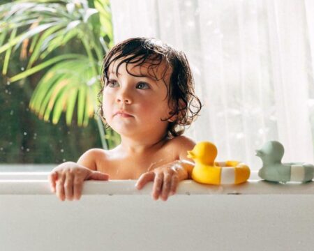 toddler in bathtub with bath toys