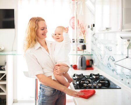 caucasian mom with baby in her arms cleans the kitchen in the house mother restores order wipes the t20 ZYvynR