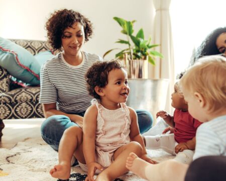 Mom friends playing with toddlers at home showing beauty of postpartum care after fourth trimester