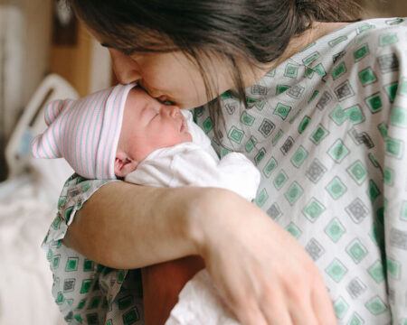mom kissing newborn baby in hospital gown