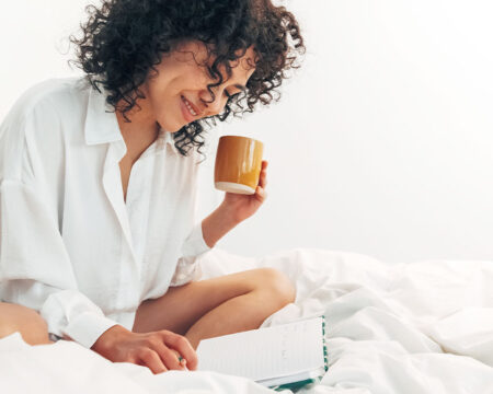 woman in bed drinking coffee and writing in guided journal