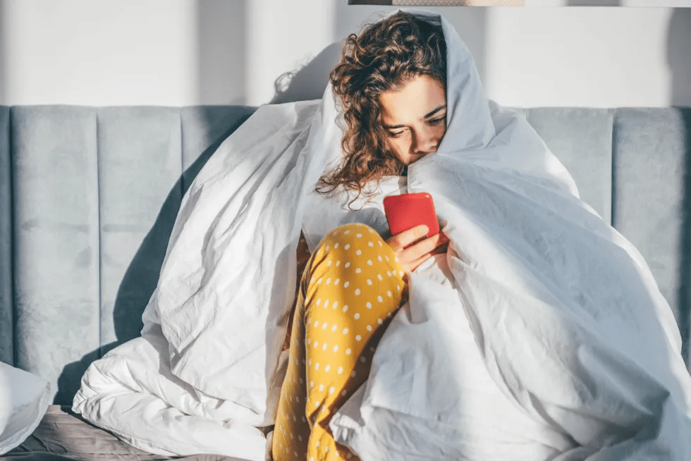 woman under bed covers looking at phone 1